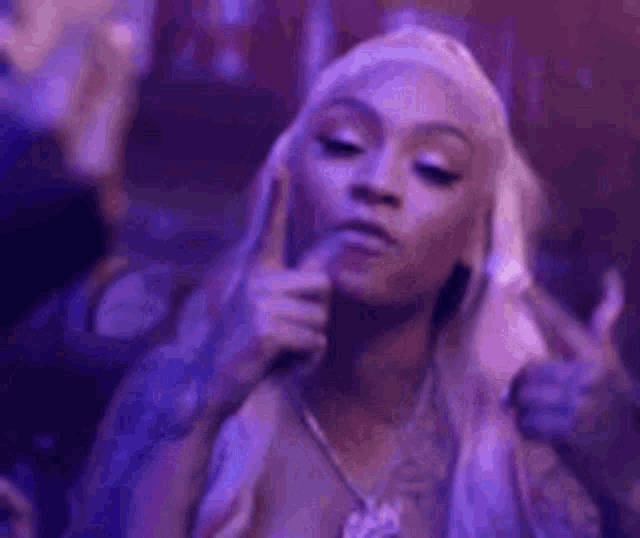 a woman with long blonde hair is giving a thumbs up sign in a club .