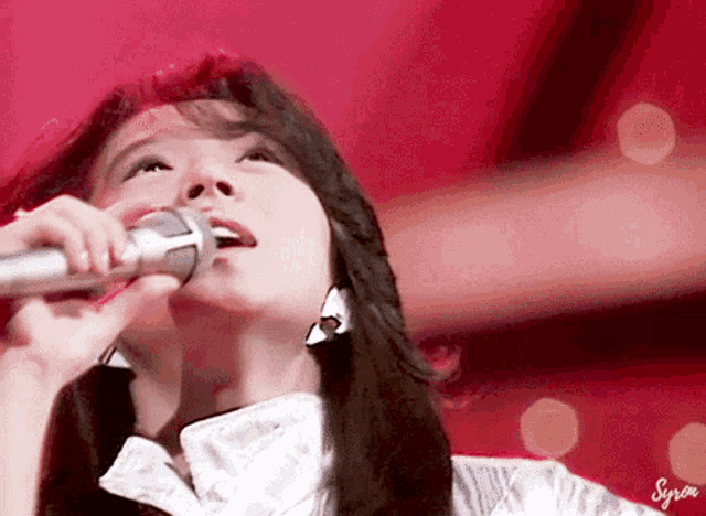 a close up of a woman singing into a microphone with syria written on the bottom right