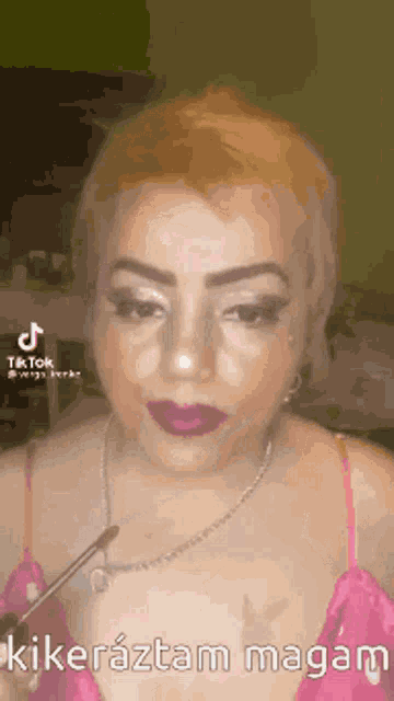 a woman in a pink dress is holding a brush in her hand and has a tiktok sticker on her face .