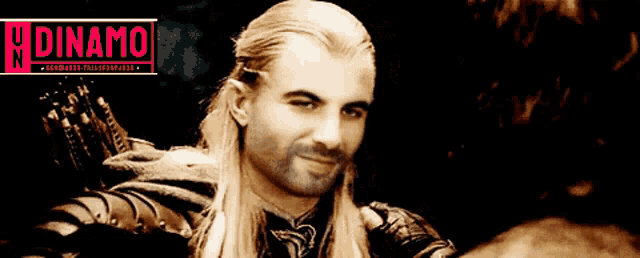 a man with long blonde hair is smiling in front of a sign that says " dinamo "