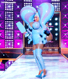 a drag queen is walking down a runway wearing a blue and purple outfit .