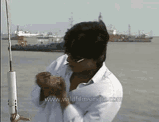 a man in a white shirt is standing in front of a body of water with the website www.wildfilmsindia.com visible