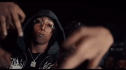 a man wearing glasses and a hoodie is taking a picture of another man with his hands .
