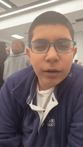 a young boy wearing glasses and a purple jacket that says ari public