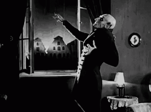 a black and white photo of a vampire standing in a living room in front of a window .