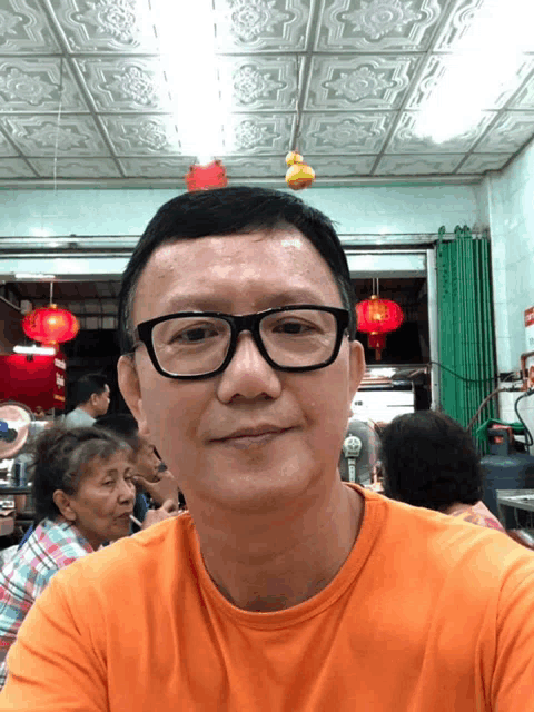 a man wearing glasses and an orange shirt sits in a restaurant