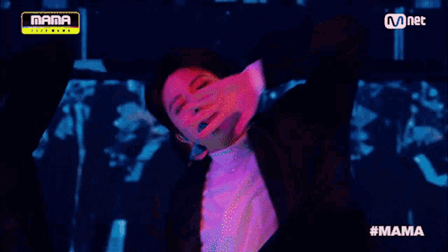 a man in a suit and white shirt is performing on a stage with a mnet logo above him