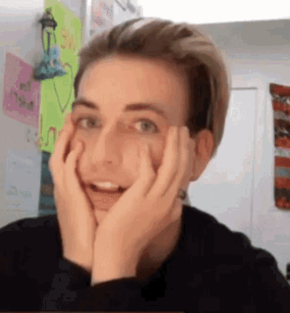 a young man with his hands on his face is smiling .