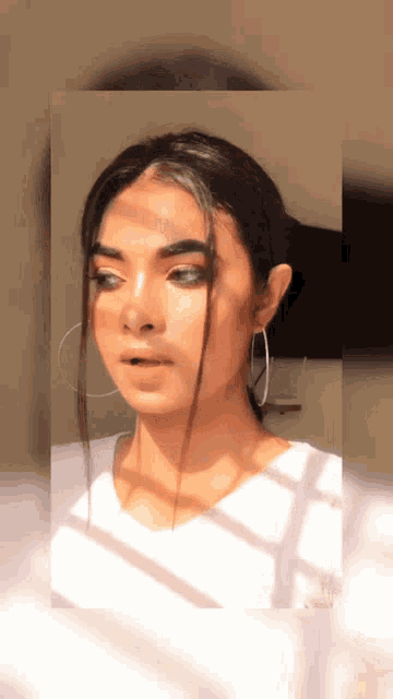 a woman wearing hoop earrings and a white shirt looks at the camera