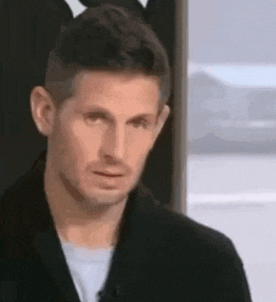 a man in a black jacket is making a funny face while standing in front of a window .