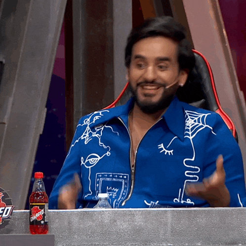 a man in a blue jacket is sitting at a table with a bottle of dr pepper in front of him