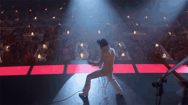 a man in a white suit is dancing on a stage in front of a crowd of people
