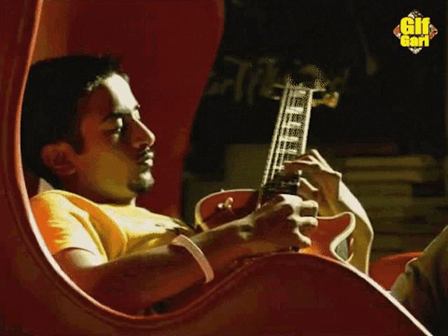 a man sits in a chair playing a guitar with the gif god logo in the corner