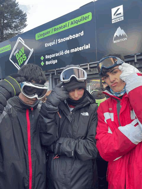 three young men wearing goggles in front of a sign that says burton