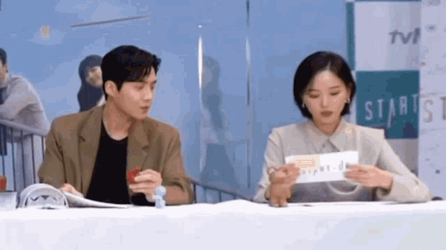 a man and a woman are sitting at a table with a sign that says start