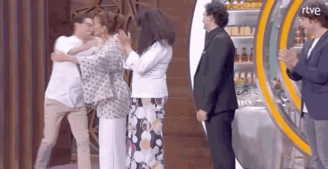 a group of people are hugging each other on a stage in a kitchen .