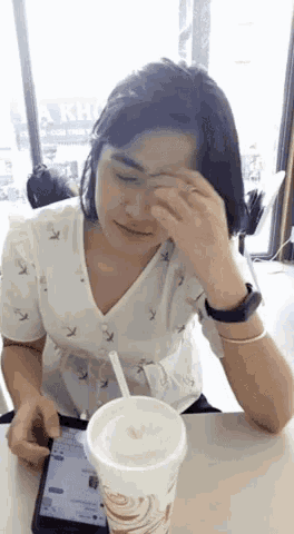 a woman sitting at a table with a cup of milkshake and a cell phone