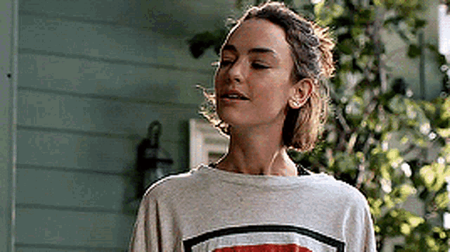 a woman wearing a striped sweatshirt is standing in front of a house with her eyes closed .
