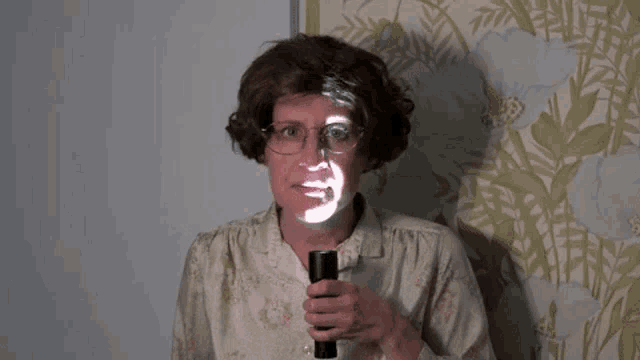 a woman with glasses is holding a flashlight with a face projected on it