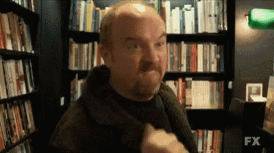 a bald man with a beard is standing in front of a bookshelf .