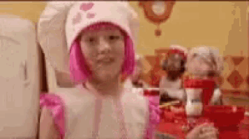 a little girl wearing a pink wig and a chef 's hat is standing in front of a table .