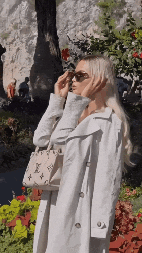 a woman wearing sunglasses and a white trench coat has a louis vuitton bag