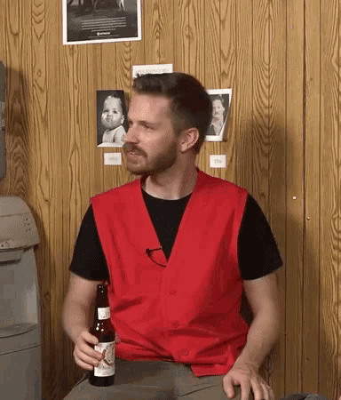 a man in a red vest is holding a bottle of beer .