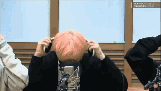 a man with pink hair adjusts his headphones in front of a mbc radio fm sign