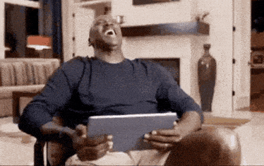 a man is laughing while holding a tablet in his hands .
