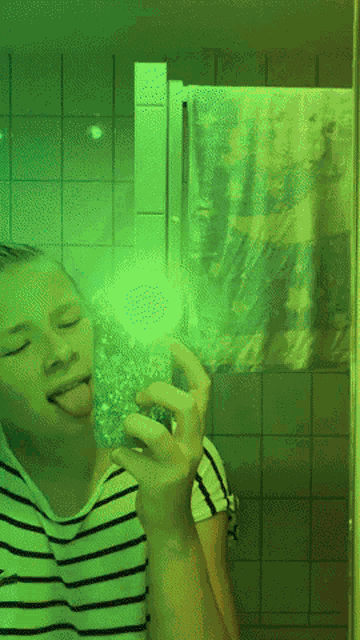 a girl in a striped shirt is sticking her tongue out in front of a mirror