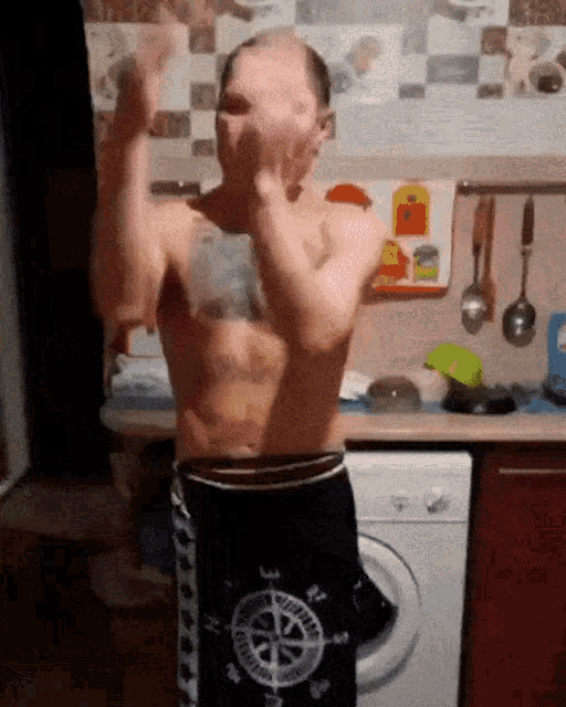 a shirtless man in shorts with a compass on them stands in front of a washing machine
