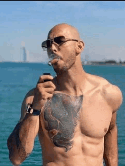 a shirtless man with a tattoo on his chest is smoking a cigar in the water .