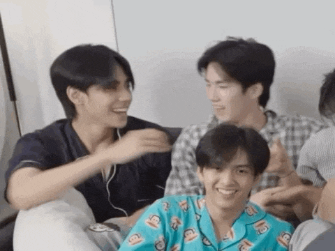 a group of young men are sitting next to each other on a couch and laughing .