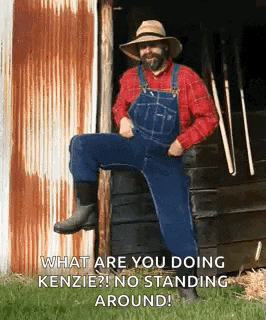 a man in overalls and a hat is sitting on a barrel and talking to someone .