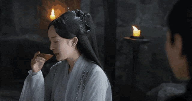 a woman in a white robe looks at a man in a room with candles