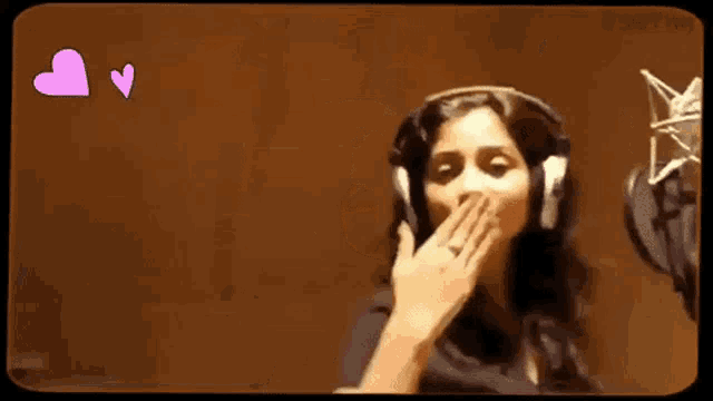 a woman wearing headphones is giving a thumbs up in front of a microphone