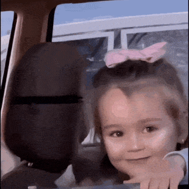 a little girl with a pink bow in her hair looks out of the window of a car