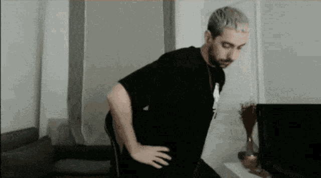 a man in a black shirt is standing with his hands on his hips in a living room .