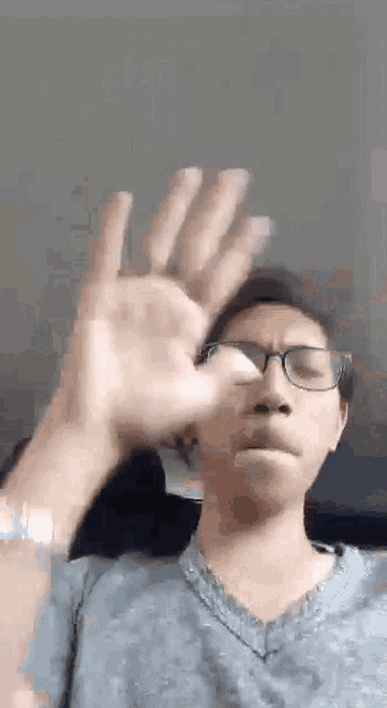 a man wearing glasses and a blue shirt is making a funny face with his hand .