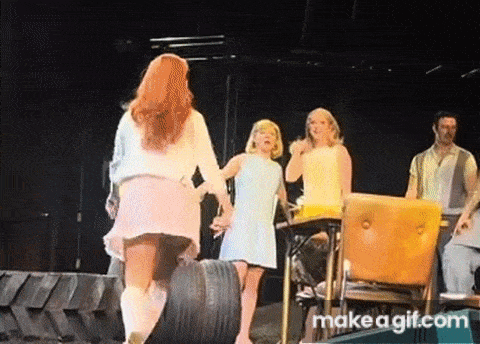 a group of women are standing on a stage with a tire in the background .