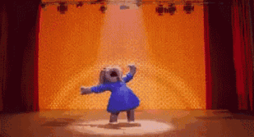 a teddy bear is dancing on a stage in a blue dress .