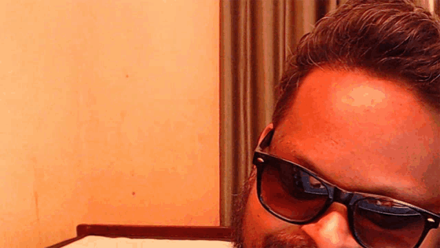 a man with a beard wearing sunglasses looks at the camera with his eyes closed