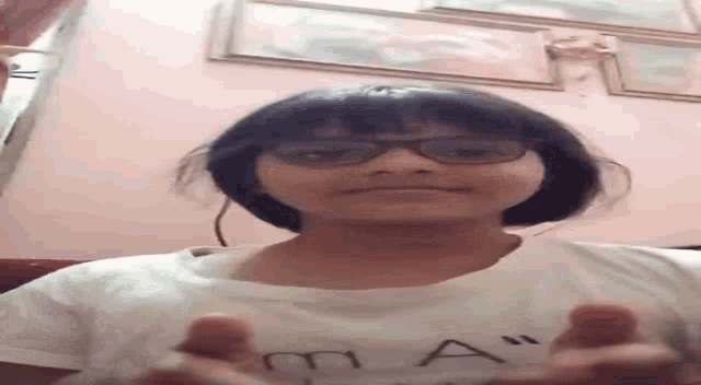 a girl wearing glasses and a white shirt is standing in a room .