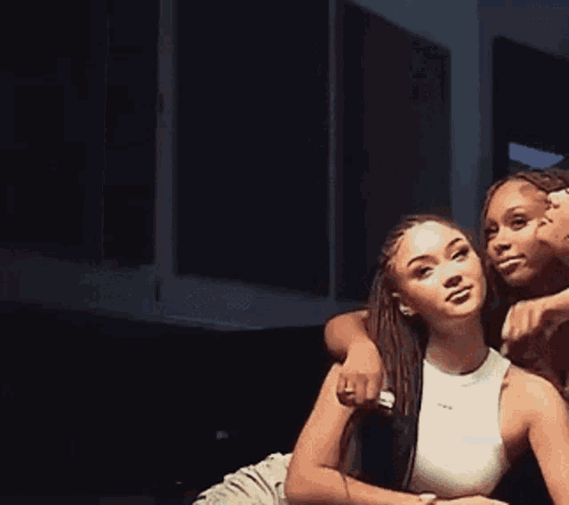 three women are posing for a picture together in a dark room . one of the women is wearing a white tank top .