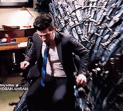 a man in a suit and tie is sitting on a chair in front of a throne