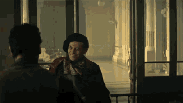 a man wearing a beret and scarf talks to another man