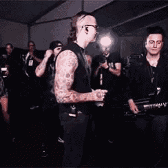 a group of men are standing in a dark room and one of them has a tattoo on his arm
