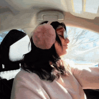 a woman wearing pink ear muffs and sunglasses driving a car