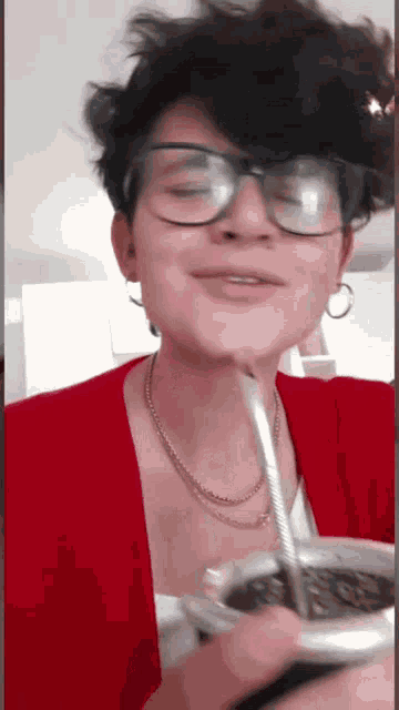 a woman wearing glasses and a red shirt is drinking from a cup with a straw