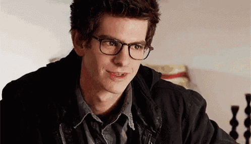 a young man wearing glasses and a black jacket is smiling while sitting at a table .